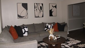 A living room with a grey sofa, black and white cushions, abstract wall art, and a coffee table with a vase and decorative items. - Serene 1-bedroom house in charming Lithonia (Lithonia)