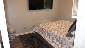 A bedroom with a bed, a television mounted on the wall, a window with blinds, and a rug on the floor. - Serene 1-bedroom house in charming Lithonia (Lithonia)
