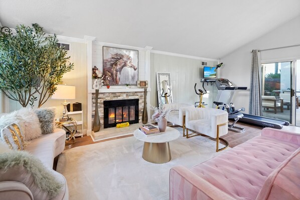A living room with a fireplace, a treadmill, a pink sofa, and a large plant. - Main House Santa Clarita Retreat+Pets with fee (Santa Clarita)