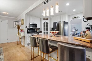 Une cuisine moderne avec des meubles blancs, un plan de travail en granit et un îlot central doté de tabourets de bar.