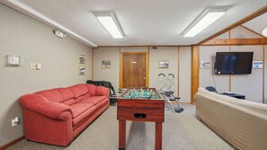 A room with a red sofa, a foosball table, a television, and a wooden door. - Twister + Little Twister Siste by Avantstay Heated Pool + Game Room + Sauna (North Creek)