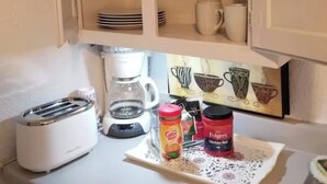 Una cocina con un armario blanco, una cafetera, un tostador y una bandeja con café Folgers y un tarro de azúcar.