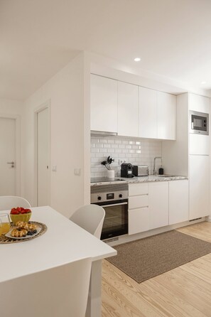 A modern kitchen with white cabinetry, a microwave, a stove, and a dining area with a table set for breakfast. - Sunshine - 2 minutes walk from the beach (Nazaré)