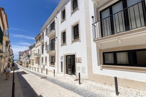 A white building with balconies, a cobblestone street, and a clear sky. - Sunshine - 2 minutes walk from the beach (Nazaré)