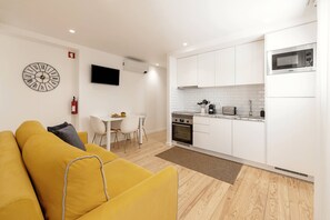 A modern kitchen with white cabinets, a microwave, and a stove. There is a dining area with a white table and chairs. - Sunshine - 2 minutes walk from the beach (Nazaré)
