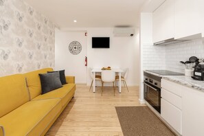A compact living space with a yellow sofa, a dining table, a kitchen area with a stove, and a mounted TV. - Sunshine - 2 minutes walk from the beach (Nazaré)