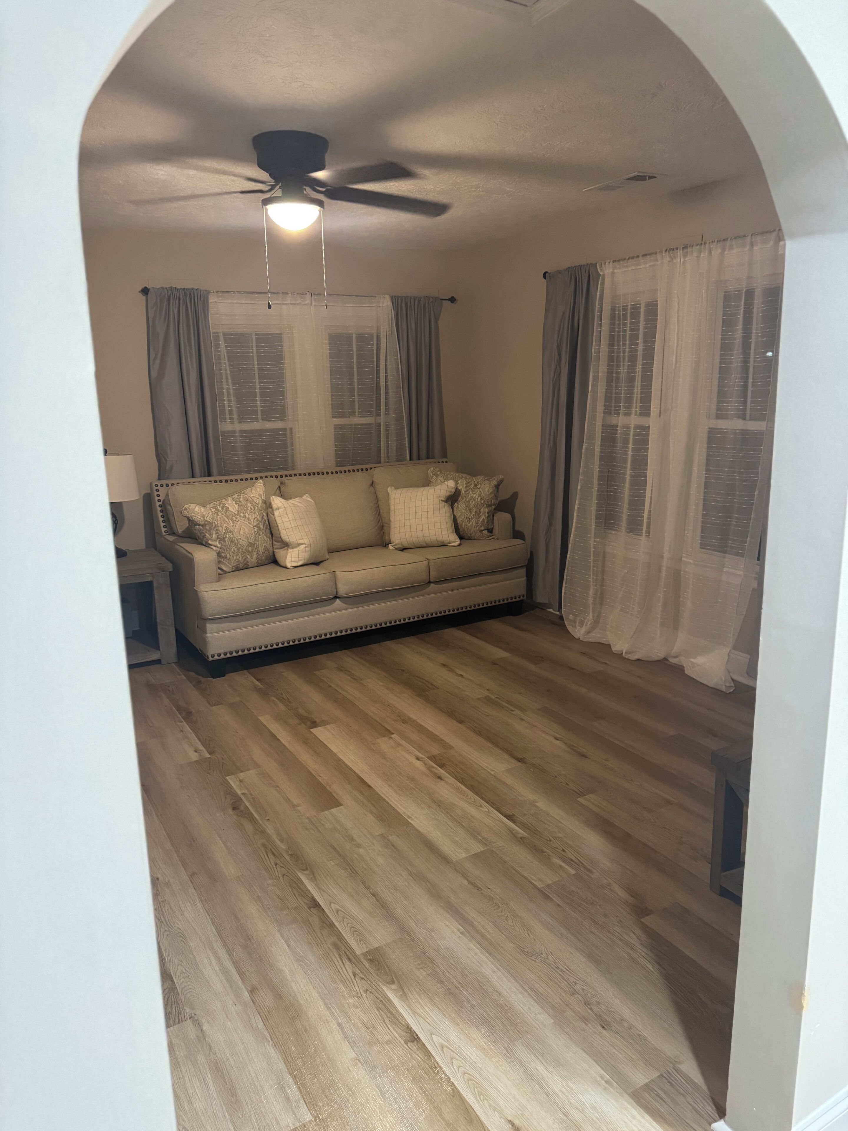 Un salon avec un canapé, un ventilateur de plafond et une fenêtre avec des rideaux.