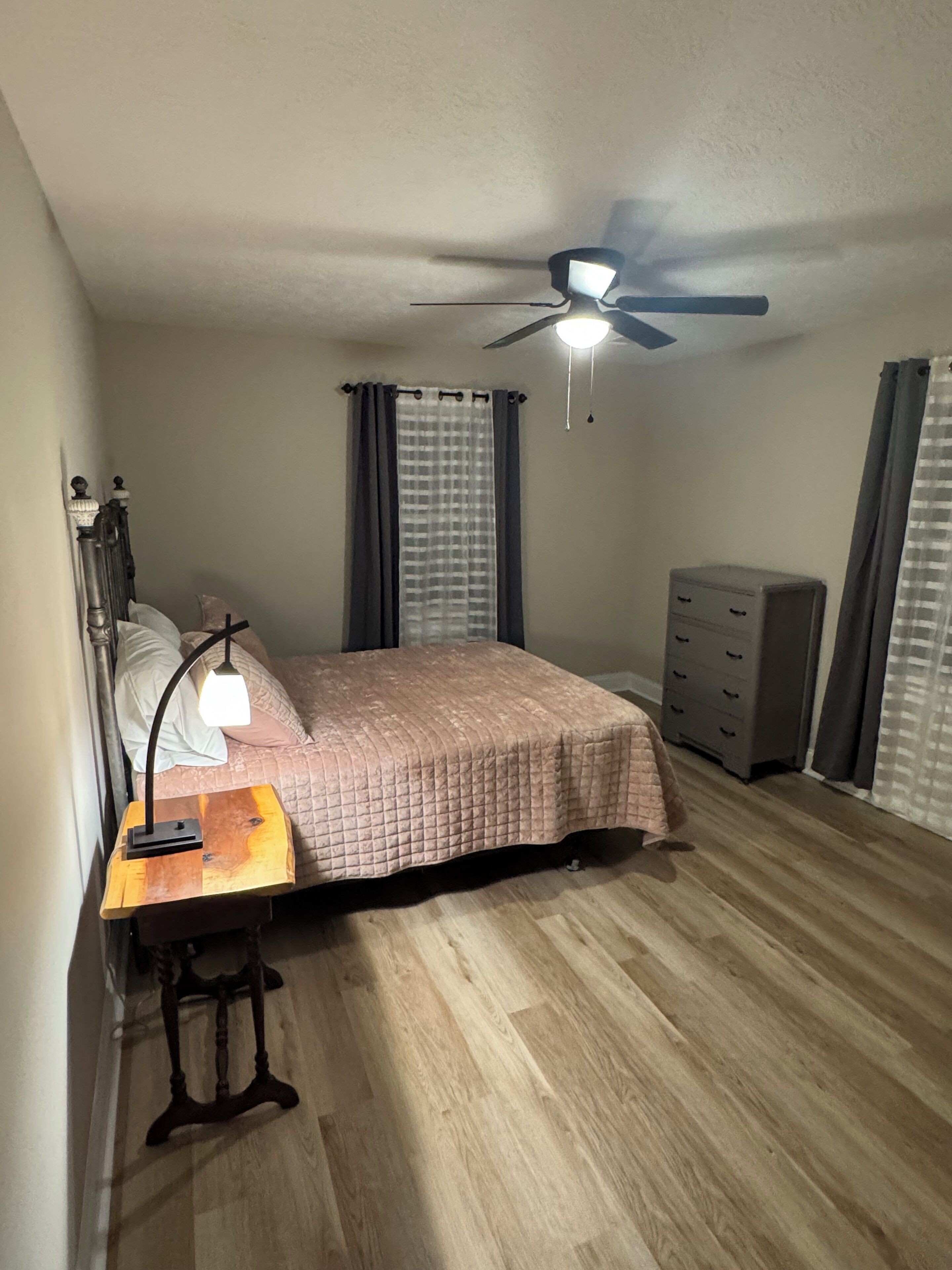 Une chambre à coucher avec un lit, un bureau avec une lampe, une commode et un ventilateur de plafond.