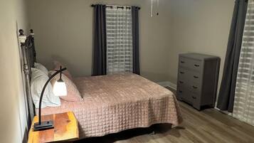 Une chambre à coucher avec un lit, un bureau avec une lampe, une commode et un ventilateur de plafond.