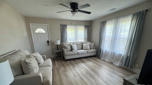 A living room with a sofa, a coffee table, a TV stand, a ceiling fan, and a door. - Close to SRP park the medical district and Fort Gordon (North Augusta)