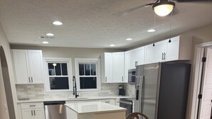 A modern kitchen with white cabinets, a central island, and a dining area with wooden chairs. - Close to SRP park the medical district and Fort Gordon (North Augusta)