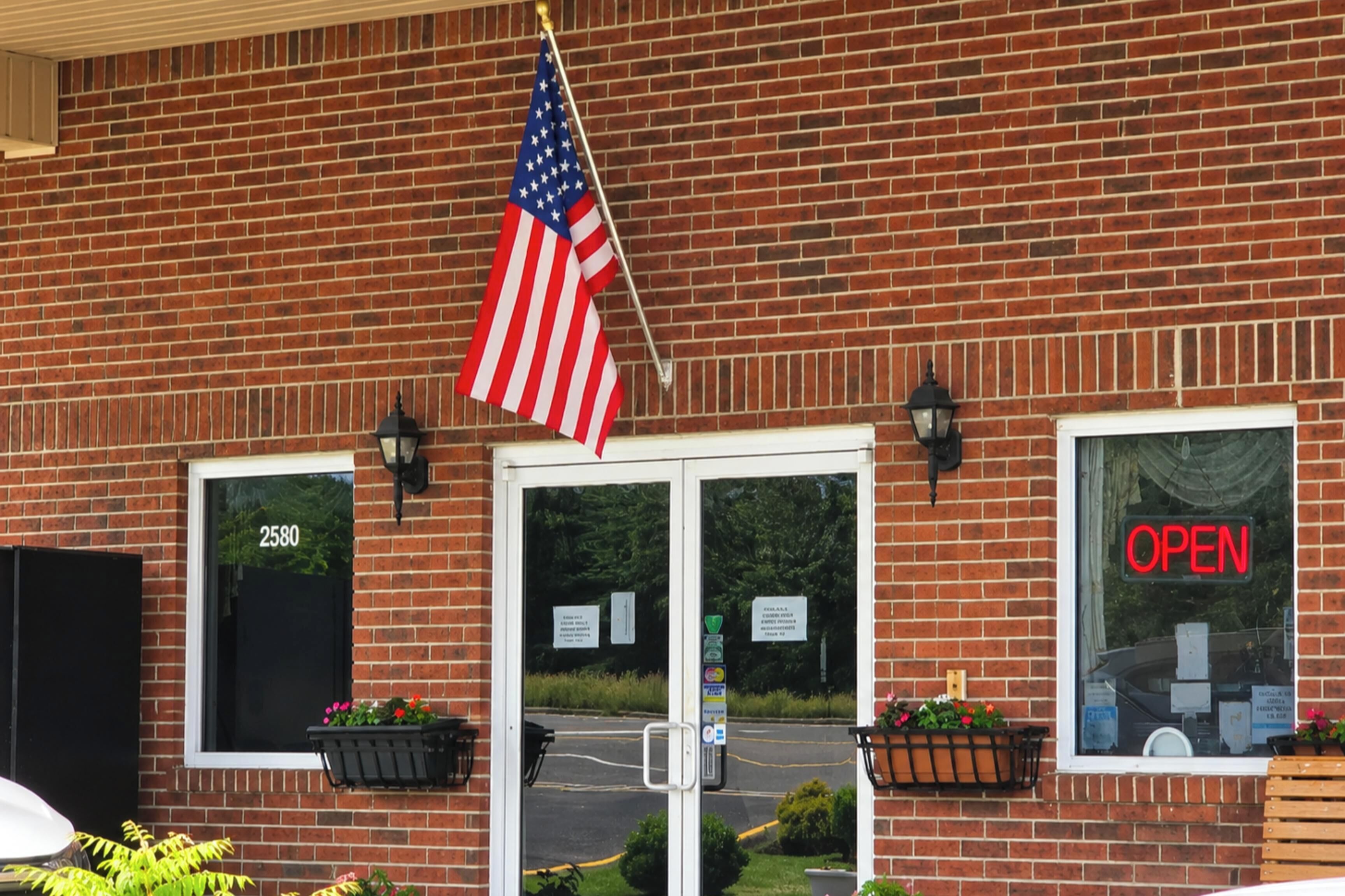 Een gebouw van baksteen met een glazen deur, een Amerikaanse vlag en een bord met de tekst 'OPEN'.