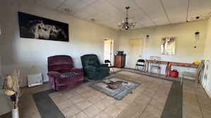 A living room with a large rug, two armchairs, a dining area with a table and chairs, and a chandelier.