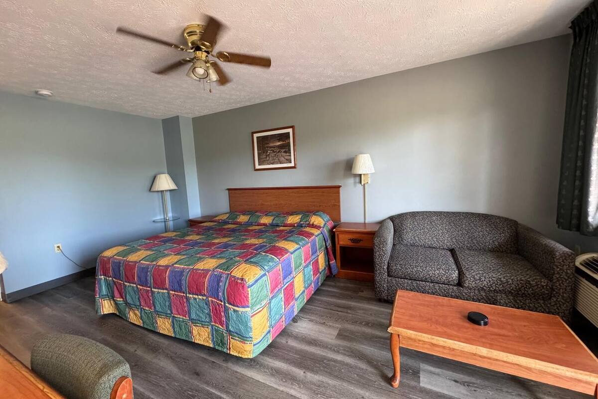 Una habitación de hotel con una cama, una silla, una mesa, un ventilador de techo y dos lámparas de noche.