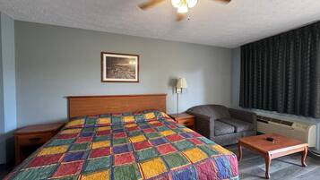 A hotel room with a bed, a nightstand, a chair, a table, a lamp, a picture on the wall, and a window with curtains.