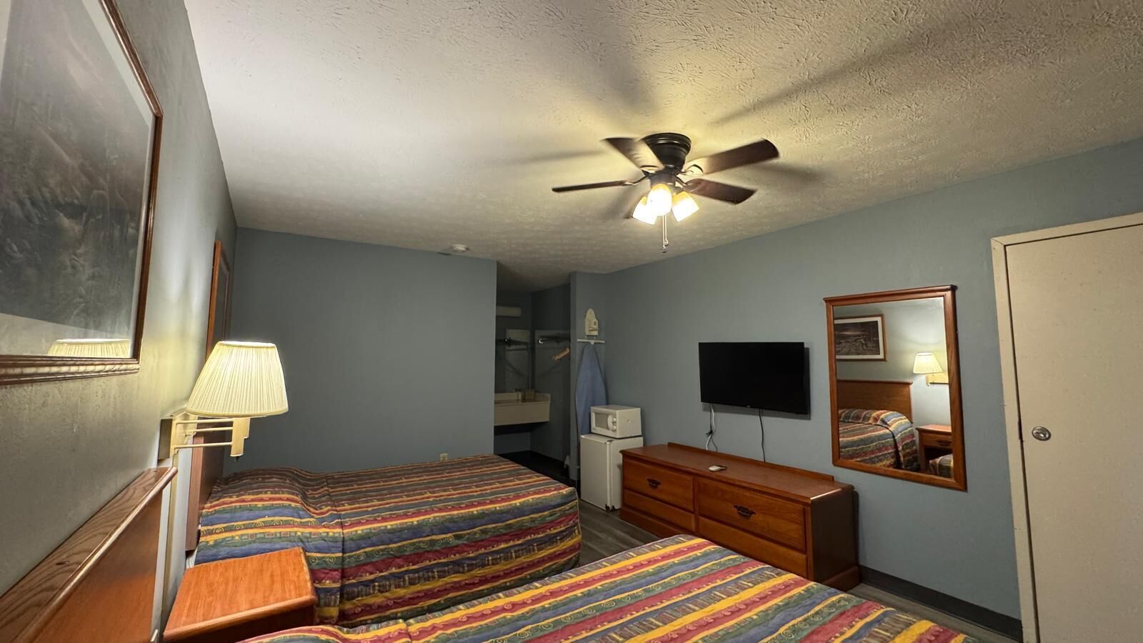 Une chambre d’hôtel avec deux lits, un ventilateur de plafond, une télévision, une commode et un miroir.