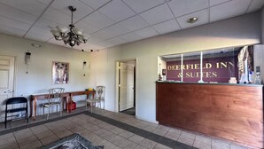 A reception area with a reception desk, chairs, a chandelier, and a door leading to another room.