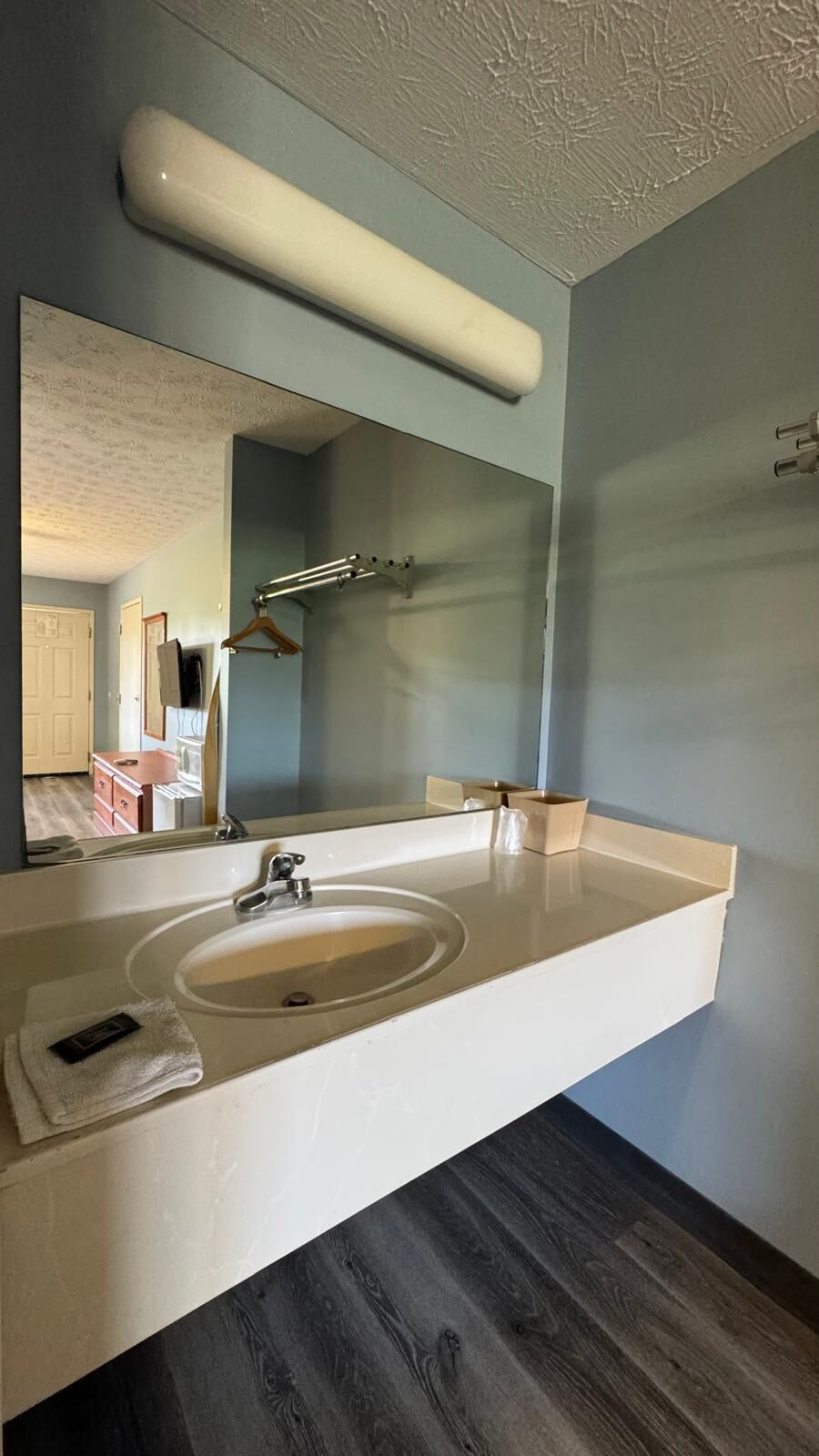 A bathroom with a large mirror, a white sink, a towel, and a wooden floor.