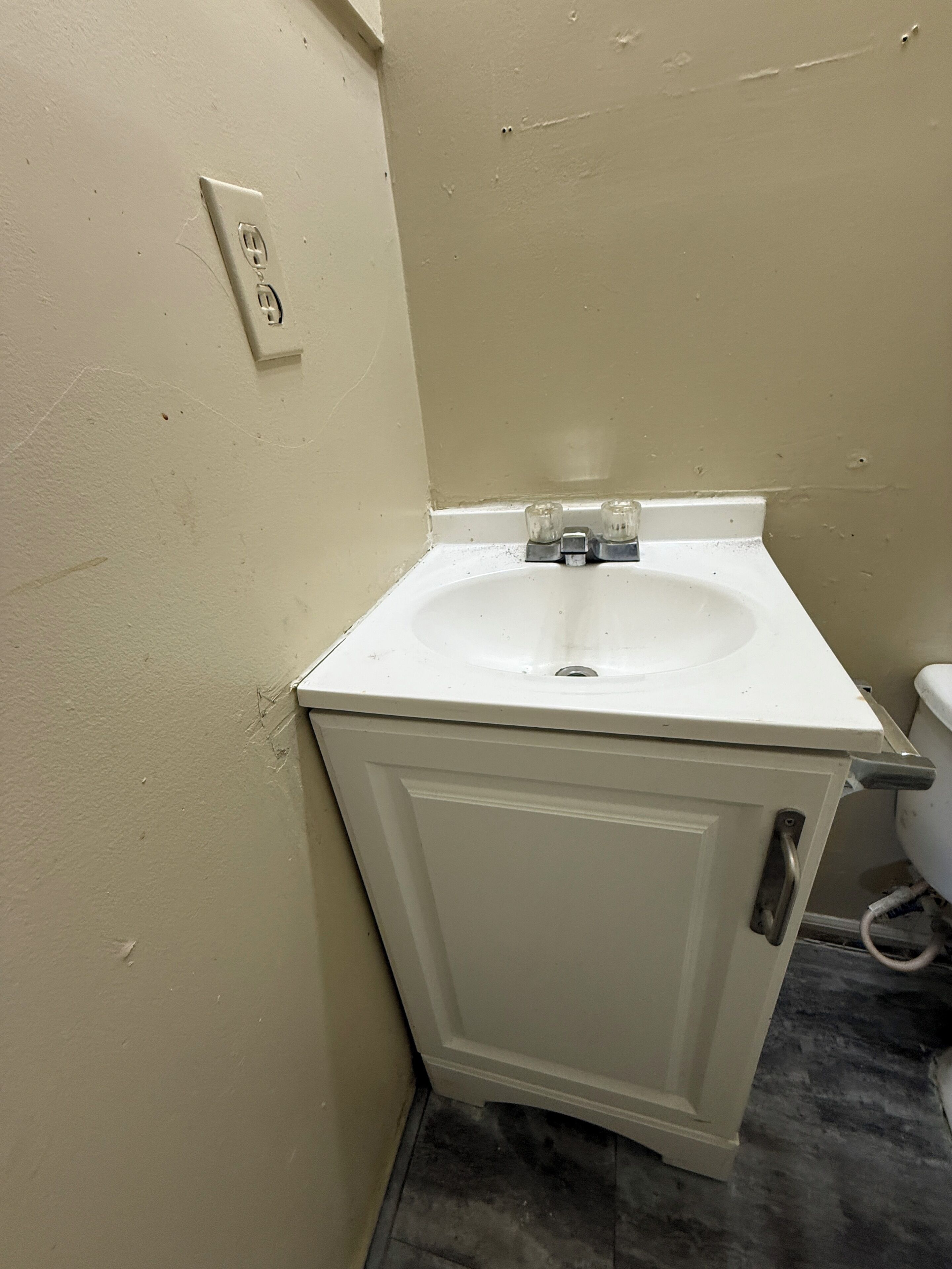 A bathroom with a white sink, a toilet, and a wall-mounted electrical outlet.