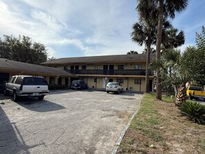 A motel with a two-story building, a parking lot, and a small garden area with palm trees. - Kings Suites & Mini Storage (Kingsland)