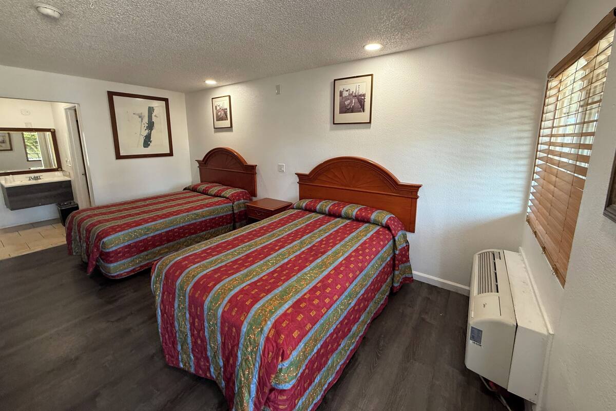 A hotel room with two beds, a bathroom, and a window with blinds.