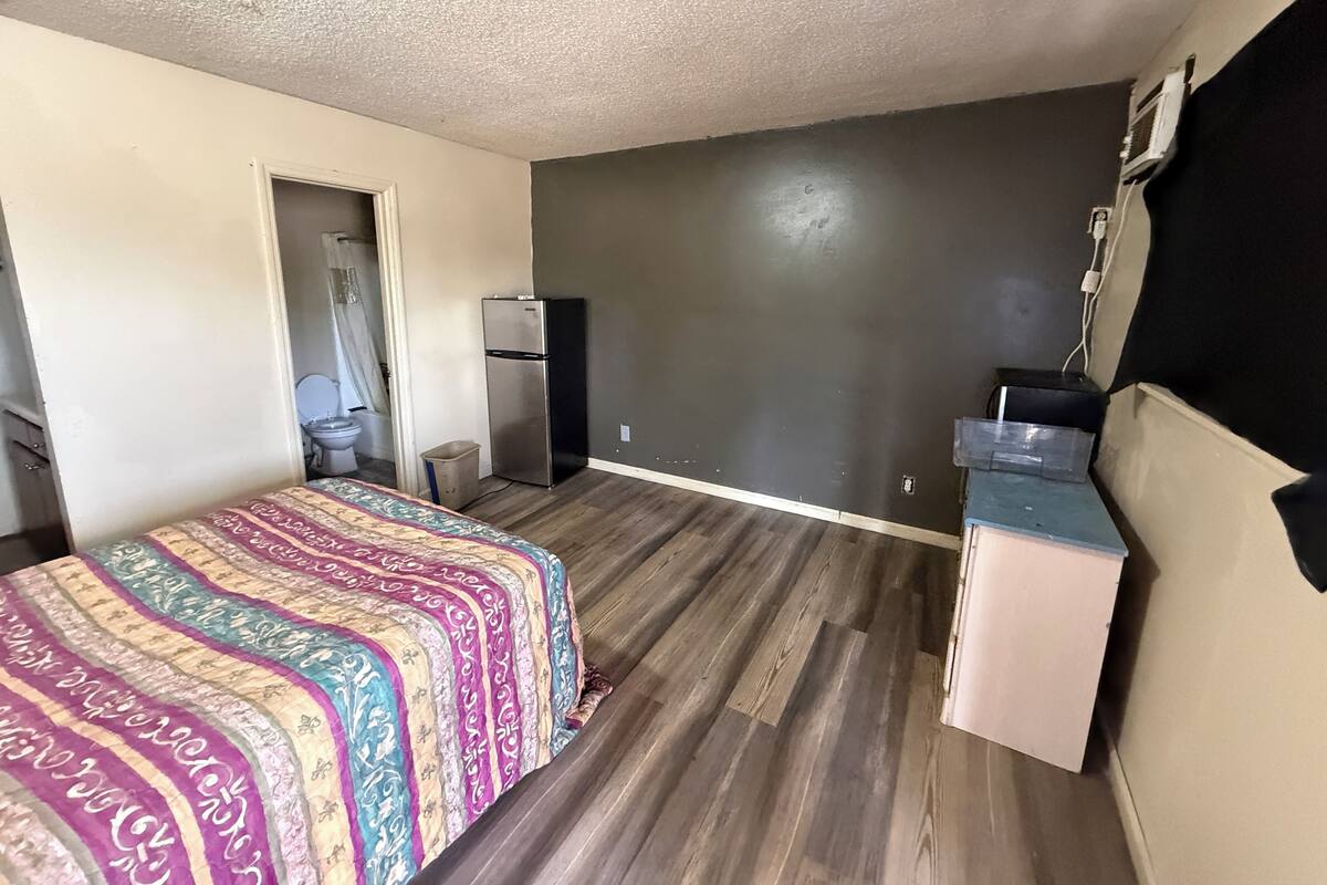 A bedroom with a bed, a refrigerator, a sink, and a mirror.