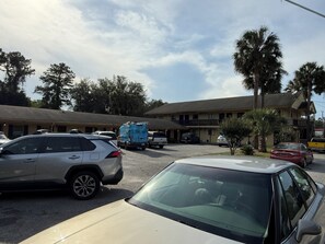 A motel with multiple parking spaces, a building with a balcony, and a clear sky.