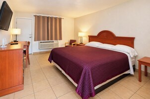 Habitación de hotel con cama, escritorio con lámpara, televisión y aire acondicionado.