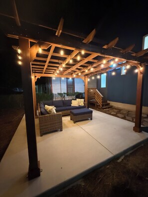 Eine Terrasse im Freien mit einer Holz-Pergola, Lichterketten, einer Couch und einer gepolsterten Bank.