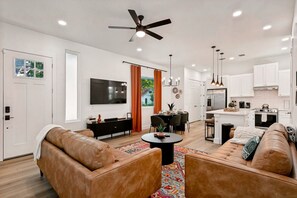 Ein modernes Wohnzimmer mit Ledersofas, einem Fernseher und einem Essbereich mit Tisch und Stühlen.