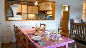 Un coin repas avec une table dressée pour quatre personnes, une cuisine à l’étage et une rambarde en bois en arrière-plan.