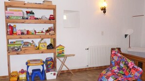 Une pièce avec une bibliothèque en bois remplie de jouets, une petite table pliante, une chaise colorée et un radiateur.