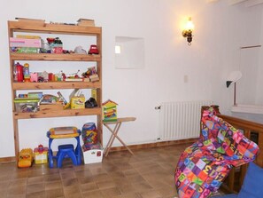 A room with a wooden bookshelf filled with toys, a small folding table, a colorful chair, and a radiator. - Sainte Germaine Vacation Rental "La Ferme (8 people)" (LUC)