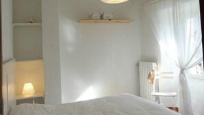 Une chambre à coucher comprenant un lit, un luminaire suspendu, une étagère avec des boîtes de rangement, un radiateur et une fenêtre avec des rideaux.