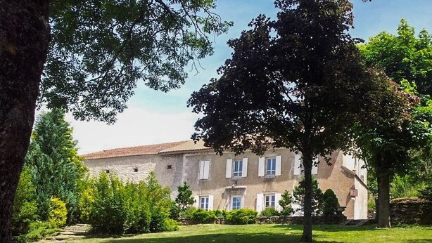 Un grand bâtiment doté d’un toit en tuiles, entouré d’une pelouse bien entretenue et d’arbres.