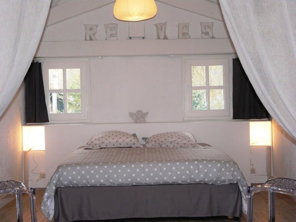 Un dormitorio con cama, dos ventanas, una lámpara de techo y un adorno en la pared.