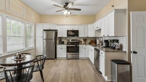 A kitchen with white cabinets, stainless steel appliances, a dining table with chairs, and a ceiling fan.
