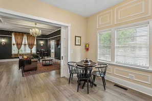 A spacious living room with a dining area, hardwood floors, and a large window with blinds.