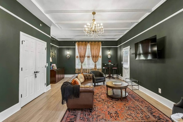 A living room with a sofa, chairs, a coffee table, a chandelier, and a TV mounted on the wall.