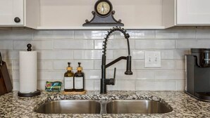 A kitchen with a stainless steel sink, a clock above the sink, and two soap dispensers on the counter.
