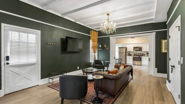 A living room with a sofa, a coffee table, and a TV. There is a kitchen in the background.