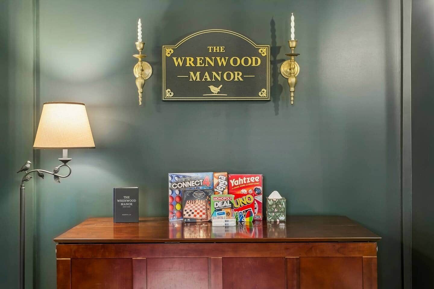 Ein Empfangsschalter mit einer Lampe, einem Schild mit der Aufschrift 'The Wrenwood Manor' und Brettspielen wie Connect 4, Monopoly und Yahtzee.