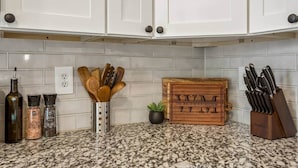 A kitchen with white cabinets, a granite countertop, a spice rack, a wooden cutting board, and a knife block.