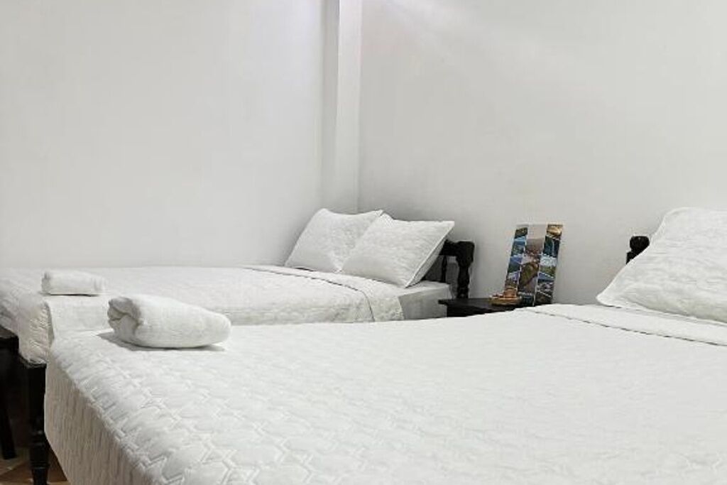 Camera d'albergo con due letti, biancheria bianca, un comodino con una lampada e un quadro appeso alla parete.
