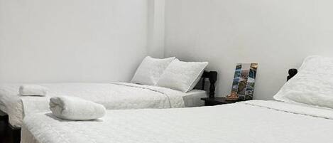 Camera d'albergo con due letti, biancheria bianca, un comodino con una lampada e un quadro appeso alla parete.