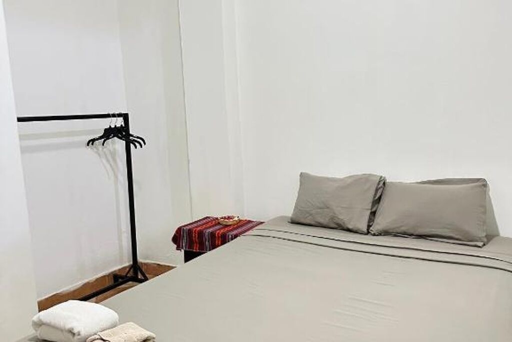 Ein Hotelzimmer mit einem Bett, einem Nachttisch mit rot-weiß gestreifter Decke und einem schwarzen Metallregal.