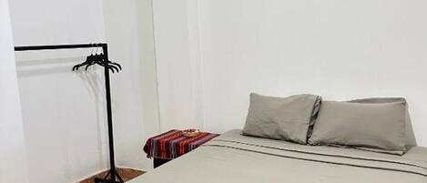 Ein Hotelzimmer mit einem Bett, einem Nachttisch mit rot-weiß gestreifter Decke und einem schwarzen Metallregal.