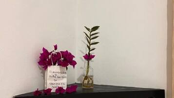 Une étagère noire avec une pancarte blanche, un vase en verre contenant une seule plante et quelques fleurs violettes éparpillées.