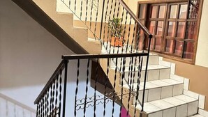 Una escalera con barandilla metálica, una planta en maceta y un ventanal de varios cristales.