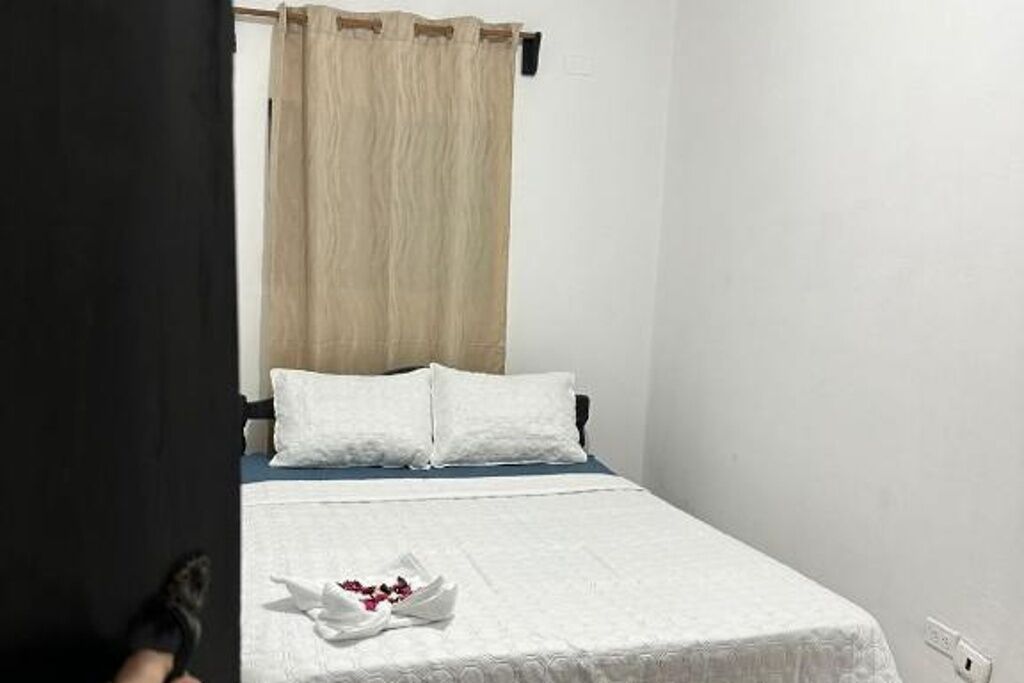 A single bed with white bedding, a beige curtain, and a white pillow on a white wall.
